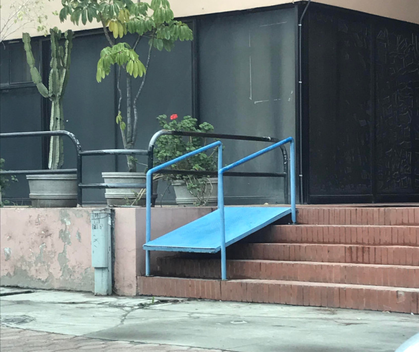 Image of a ramp placed above some stairs that has a large drop-off on the end and is completely inaccessible.